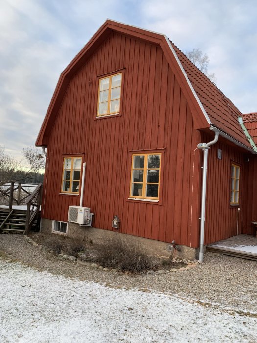 Hus från 1934 med mansardtak och rödfärgade träväggar, snöfläckar på marken.