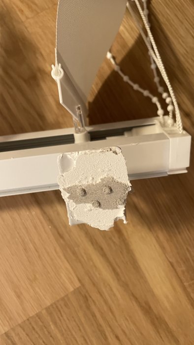 Gardinkrok fastlimmad på en målad vägg, med lossnad färg och synligt gipsmaterial.