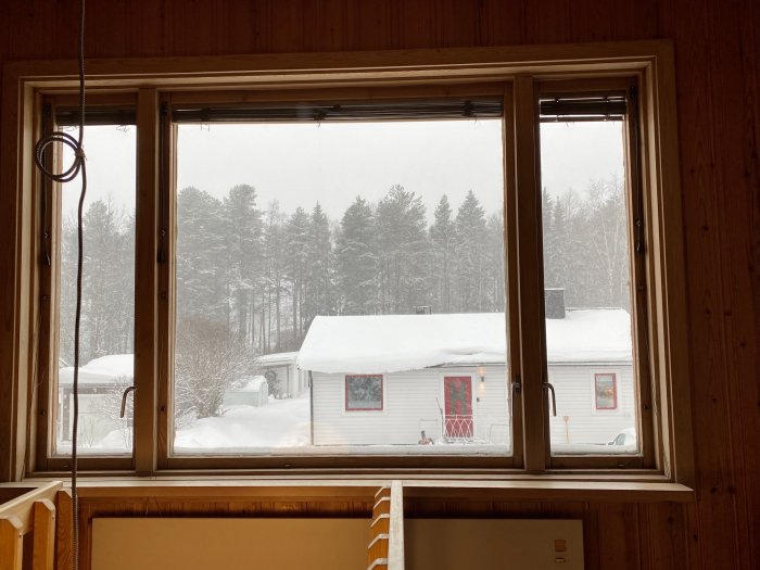 Trebent fönster med utsikt över snöig landskap och hus, indikerar dragighet och kall övervåning.