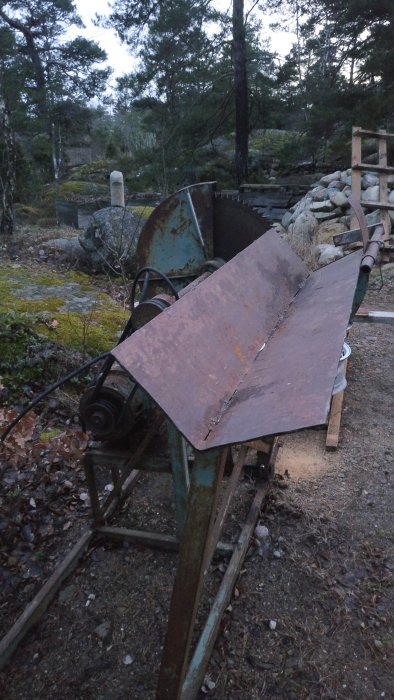 Gammal vedkap med rostig klinga och improviserad skyddsplåt utomhus, omgiven av natur.