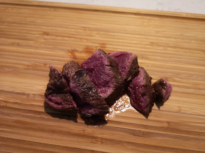 Skivat rött kött på en bambu skärbräda, förberett som mellanmål innan ugnsstekning.