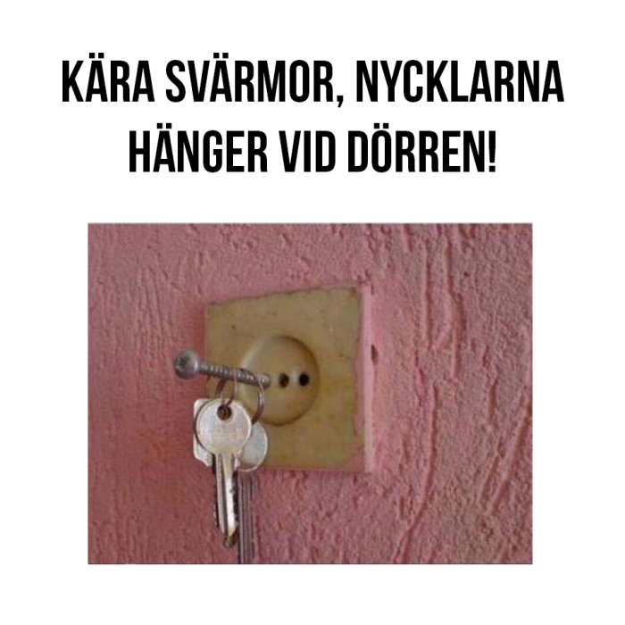 Nycklar hängande på en skruv i en rosa vägg med texten "Kära svärmor, nycklarna hänger vid dörren!