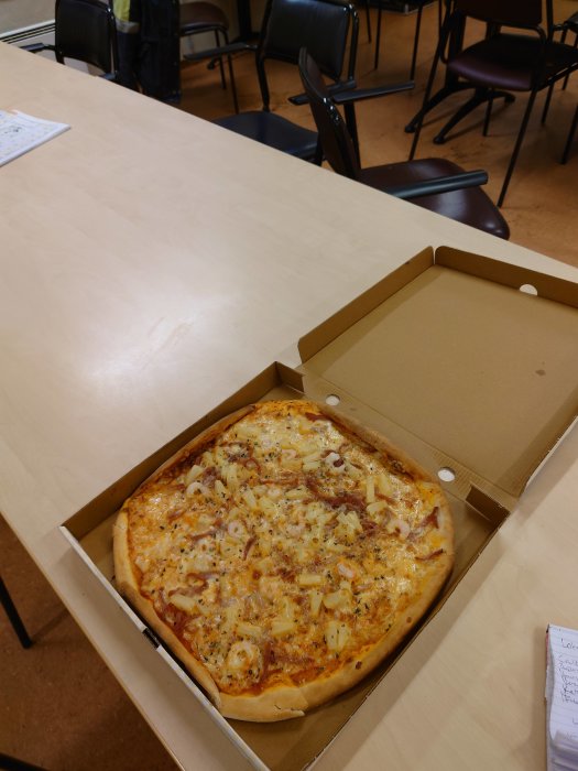 Pizza Hawaii med räkor på ett bord i en enkel matsal med bruna stolar.