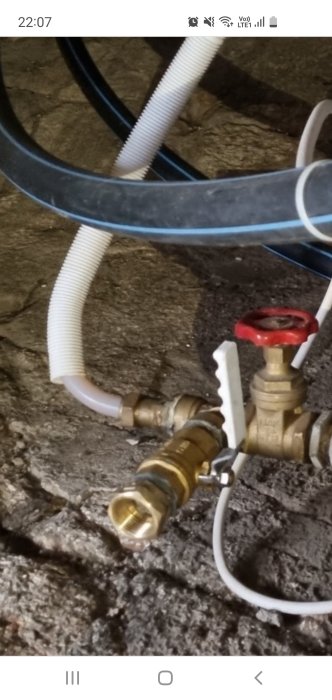 VVS-installation med pump, slangar och en röd ventil på betongunderlag.
