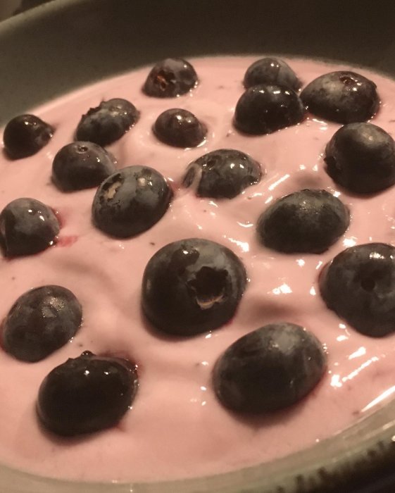 Egenodlade blåbär på toppen av rosa yoghurt i en skål, del av en lyxig helgfrukost.