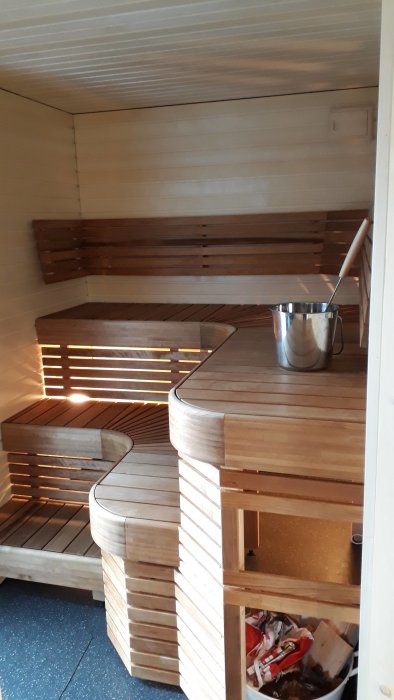 Interiör av en bastu med färdigbyggda träbänkar i olika höjder och en metallhink på översta bänken.
