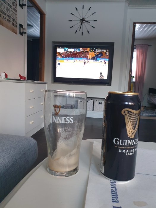 Vardagsrum med en hockeysändning på TV, ett tomt Guinnessglas och en Guinnessburk på ett bord.