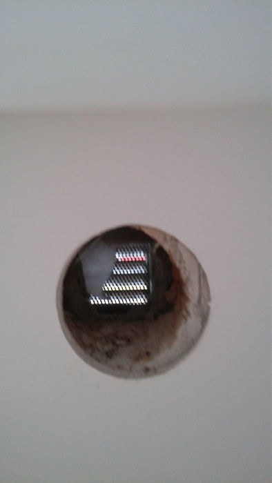 Hål i en vit vägg som visar lite av den yttre miljön genom en rutmönstrad barriär.