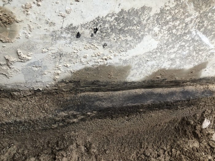 Betonggolv i källare med tydlig avgränsning mellan den grova betongytan och det underliggande lagret av grus.