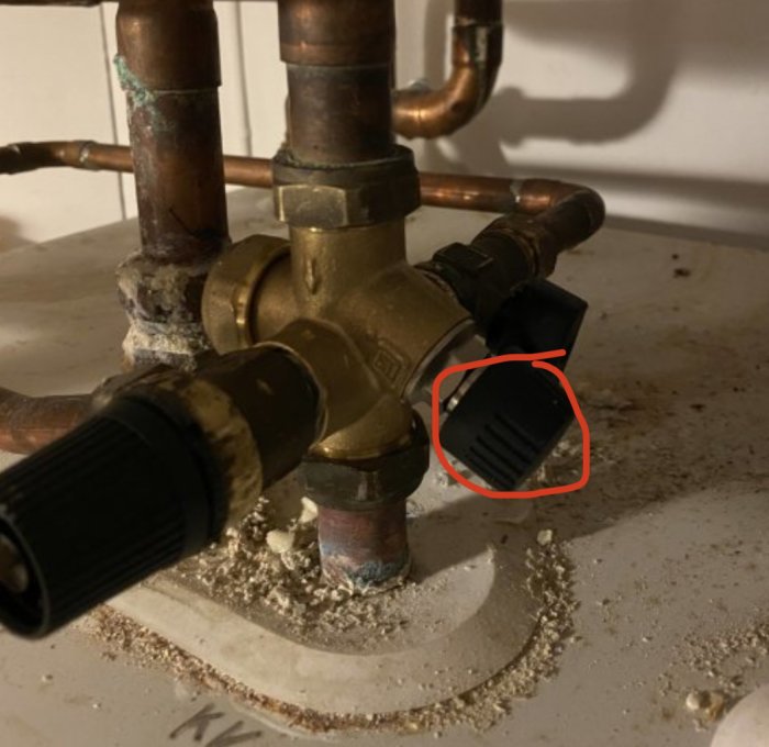 Rörkopplingar och ratt på värmesystem, inringad ratt med fokus på dess skruvfunktion.