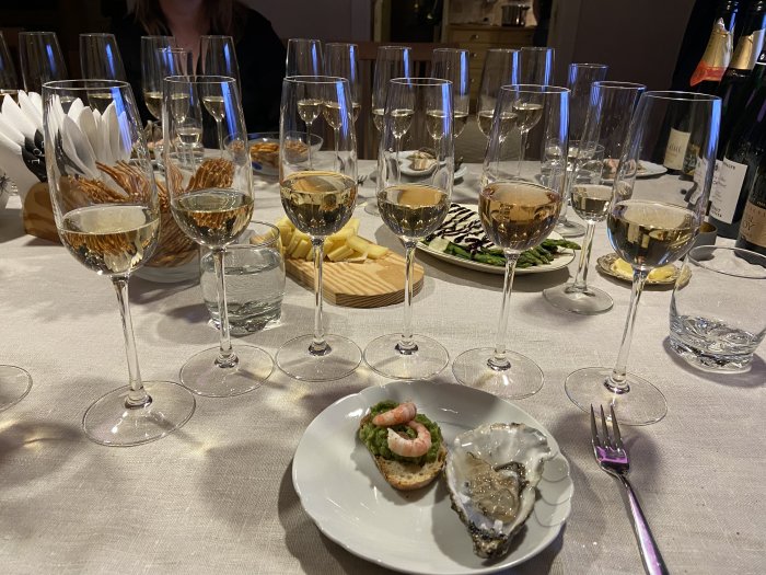 Festligt dukat bord med vin i glas, skaldjur på liten tallrik och bakomliggande förrätter.