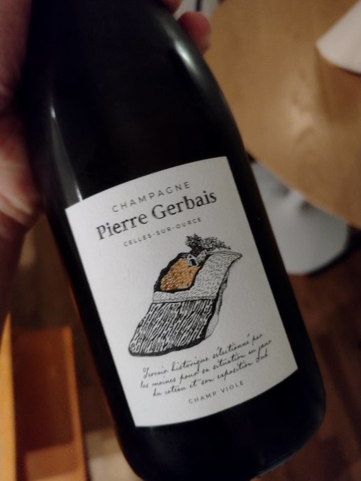 Hand håller en flaska Champagne Pierre Gerbais med etikett som avbildar en vinranka.
