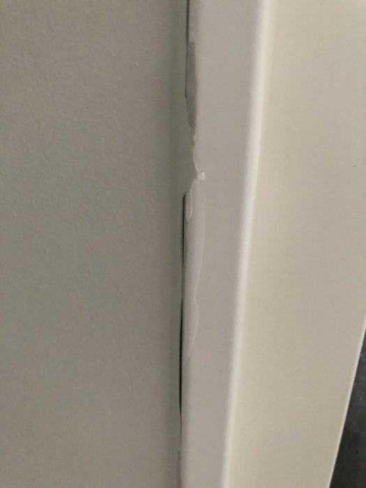 Närbild av en vägg med dåligt utförd skarv där tapet ser slarvigt skuren ut och bubblar upp vid en dörrkarm.