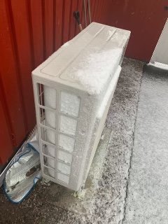 Värmepump utomhus täckt med snö vid kylig temperatur.