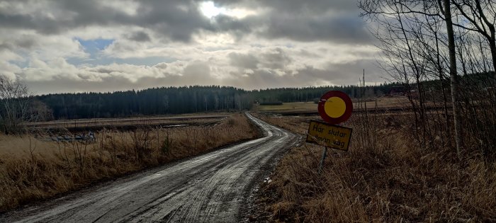 Grusväg på landsbygd med skylt som anger slutet på allmän väg under molnig himmel.