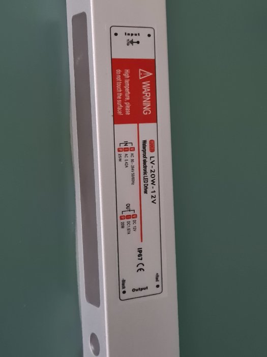 Etikett på en badrumsspegels belysningsdrivenhet som visar varningstexter och tekniska specifikationer.