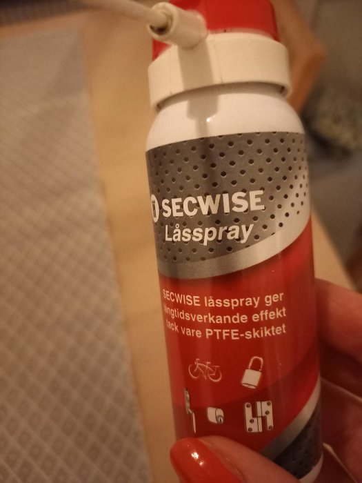 Hand håller en burk SECWISE låsspray med text om långtidsverkande effekt tack vare PTFE-skiktet.