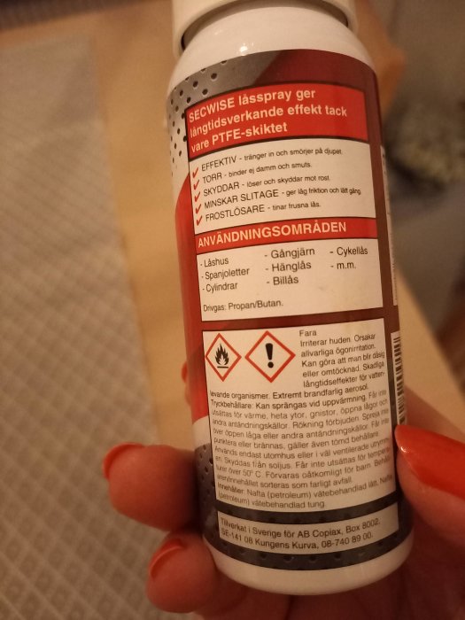 Hand håller en burk med smörjspray, etiketten visar varningsikoner och information om produkten.