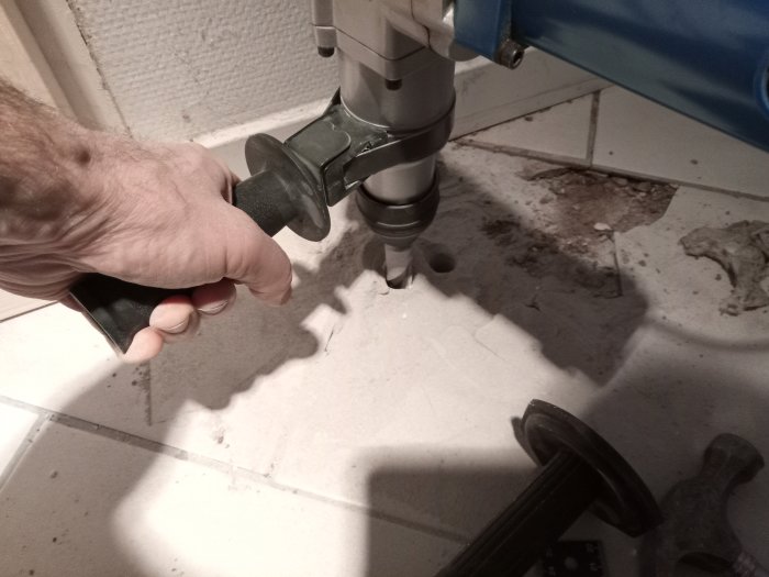 Användning av en stor borr för att borra genom betong och frigolit, med borrspån på golvet.