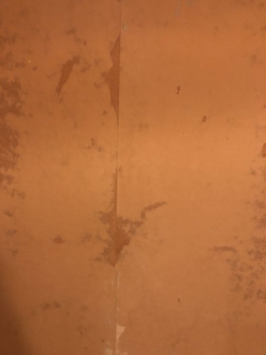 Vägg med ojämnheter och rester av tapet på ett plywoodunderlag i renoveringsprojekt.