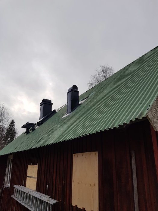 Nyinstallerad plåthuv för ventilation på ett hus med grön vågplåtstak.