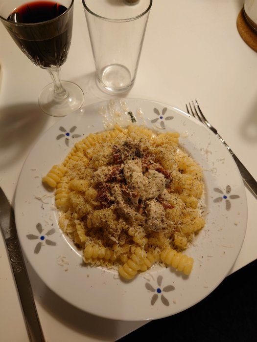 Pasta med soltorkade tomater, basilika, riven parmesan och svartpeppar på tallrik bredvid glas vin.