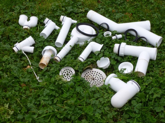 Samling av vita VVS-delar och rördelar utspridda på grön gräsmatta, tecken på åldring och användning.
