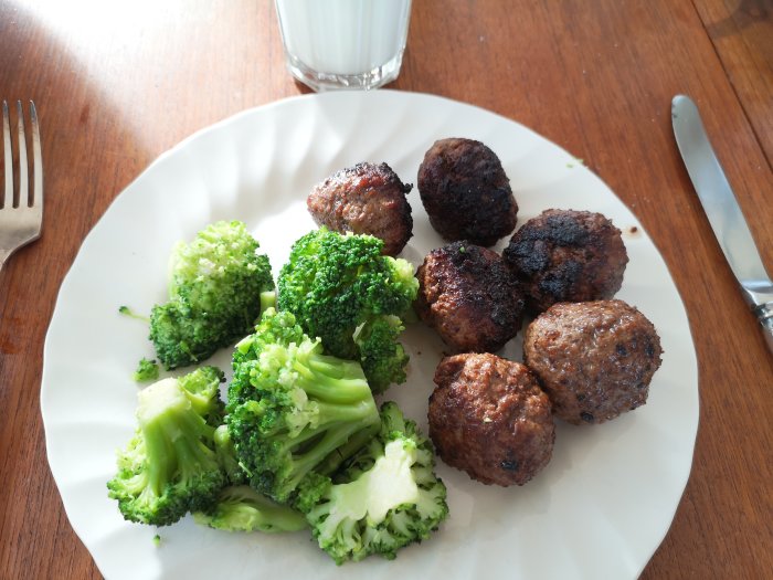 Hemlagad lunch bestående av köttbullar och ångkokt broccoli på en tallrik med en gaffel och glas mjölk.