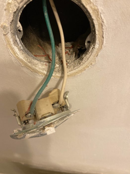 Ett öppnat hål i en vägg med synliga elledningar och en gammal, skadad elektrisk dosa som behöver repareras.