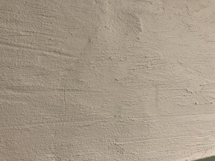 Nyputsad vägg med grov och ojämn struktur, visar en större reparerad spricka.