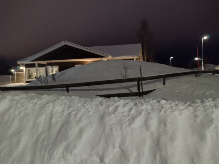 Insynsskydd byggt av träplankor framför ett snötäckt hus på kvällen.