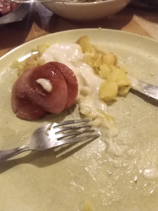 Kokt och stekt korv med mosad potatis och pepparrotsås på en tallrik med en gaffel.