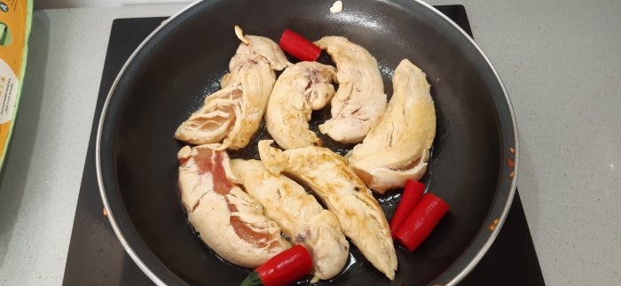 Stekande kycklingfiléer i en panna med röda chilipeppar, ingrediens till Chicken a la Teide recept.