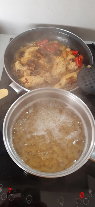 Kyckling a la Teide med champinjoner och röd chili i stekpanna, kokande pasta i kastrull.