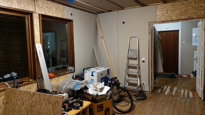 Renoveringsrum med OSB-skivor och gipsväggar, isoleringsmaterial, verktyg och byggmaterial syns.