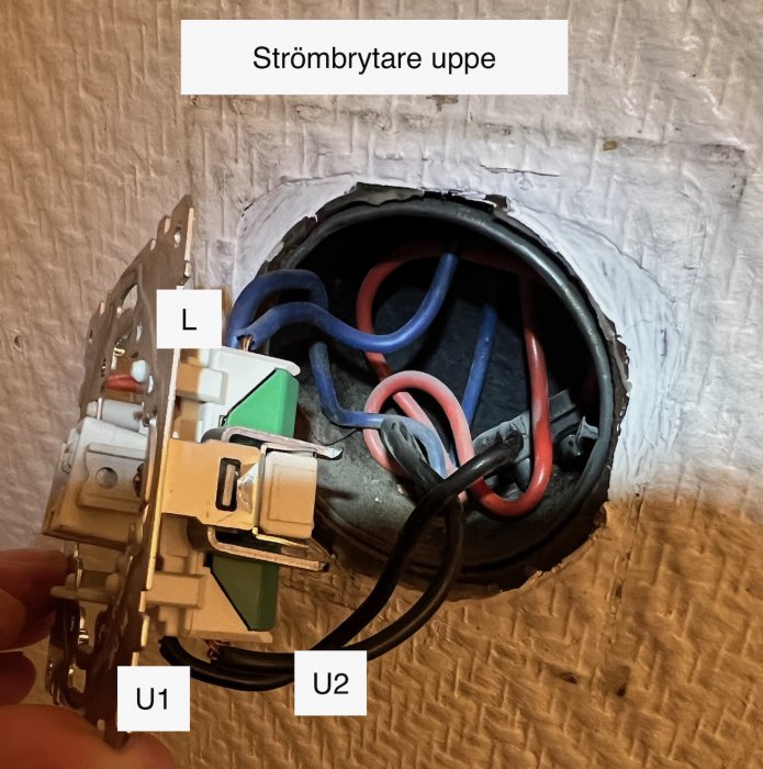 Strömbrytare med märkta kablar L, U1 och U2 urkopplad ur väggdosa med synliga blå och röda elledningar.