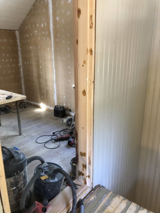 Renovering av dörröppning med spackelvägg och dörrkarm som behöver reparation, samt verktyg på golvet.