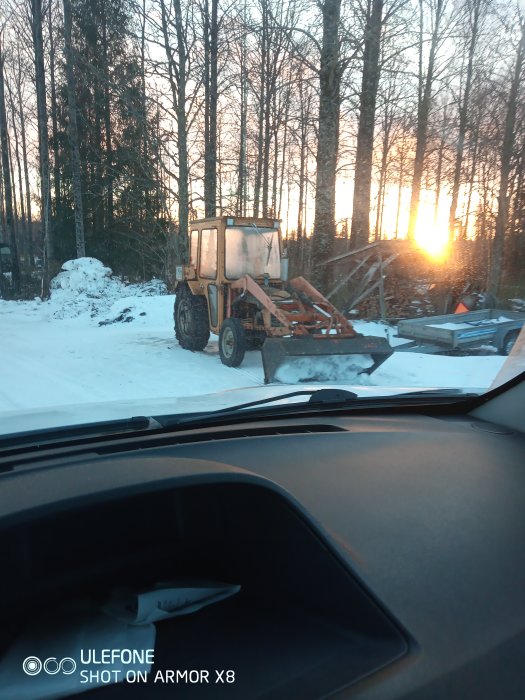 En gulnad Leyland 154 traktor från 1978 parkerad i ett vinterlandskap vid solnedgång, sedd genom en bilruta.