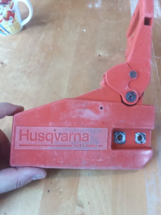 Röd kåpa med texten "Husqvarna Made in Sweden" hålls av en hand, synliga användningsspår trots ålder.