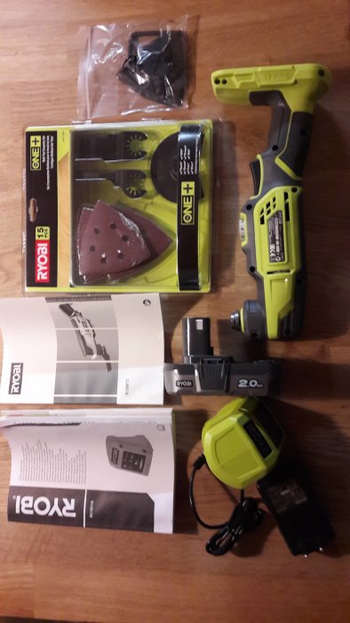 Sladdlös slipmaskin från Ryobi med gul och grön design, 2,0 Ah batteri, laddare och sandpapper på träbord.