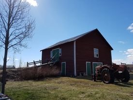 Gamla stora röda ladugårdsdel i lantlig miljö med sjunkande grund, vid sidan om en traktor.