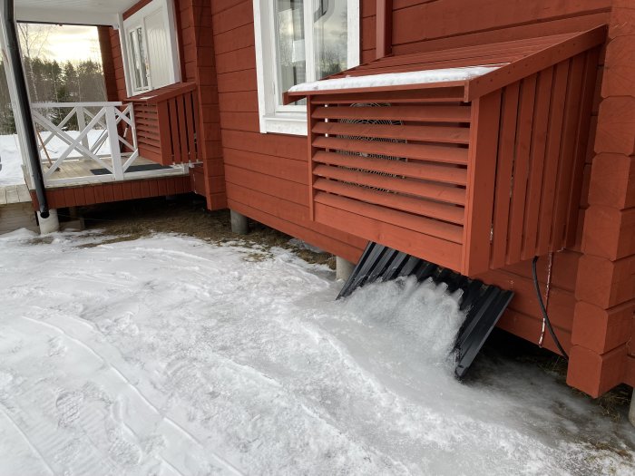 Två luftvärmepumpar installerade utomhus på rött hus, högra pumpen med betydande isbildning och kondensvatten på marken.