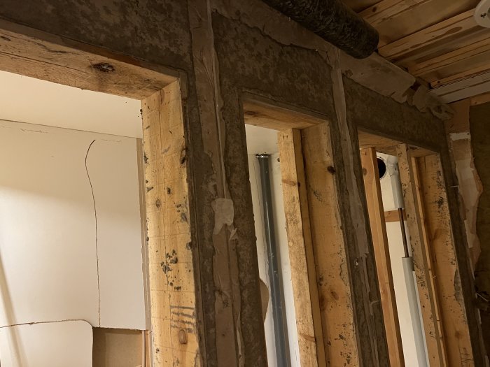En delvis riven vägg med trästolpar och synliga betongpelare och en horisontell betongbalk i ett pågående badrumsrenoveringsprojekt.