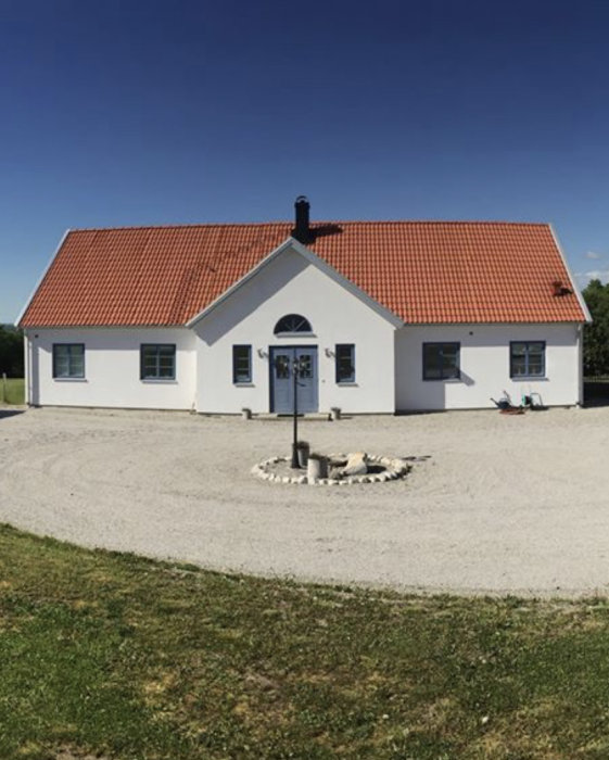 Vit enplansvilla med rött tegeltak, uppfart och gräsmatta, byggt av örementhus.