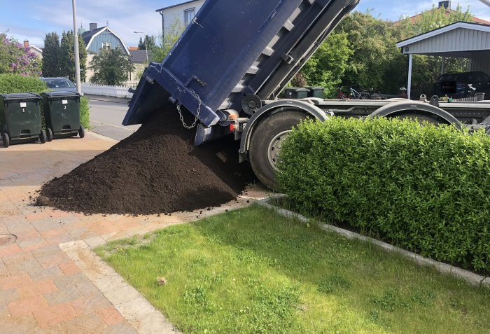 Lastbil tippandes ut jord på en uppfart vid en bostad, troligen för trädgårdsprojekt.