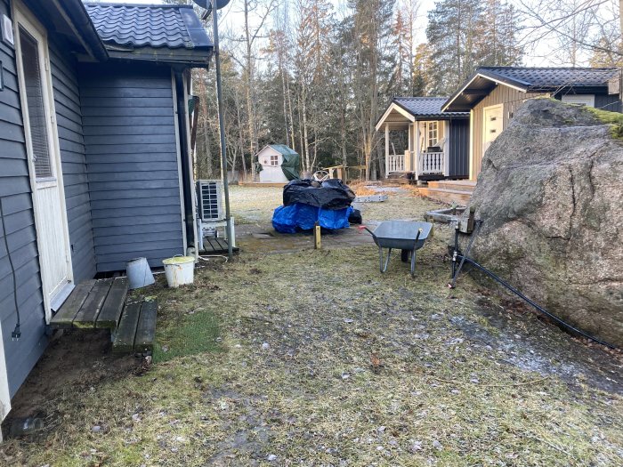 Bakgård med befintligt träträdäck, stuga, skottkärra och stor sten, utrymme för ny altanbyggnation.