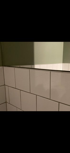 En toalettspegel monterad ovanför kakel med synlig glipa i nederkanten.