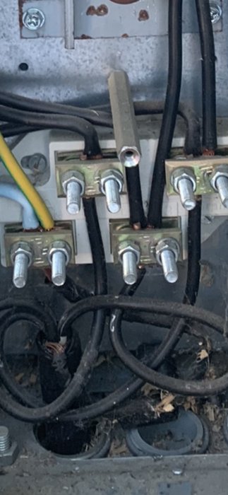 Elektrisk anslutning i fasadmätarskåp med olika kablar anslutna till tre plintar, viss isolering i svart tejp.