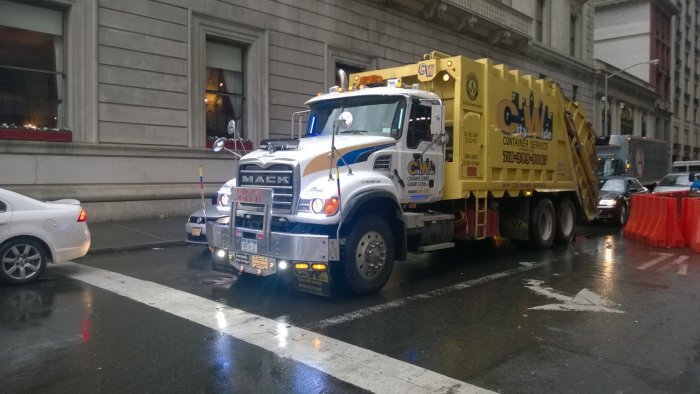 En iögonfallande gul och vit sopbil på en våt gata i New York med skylten "City Wide Container Service".