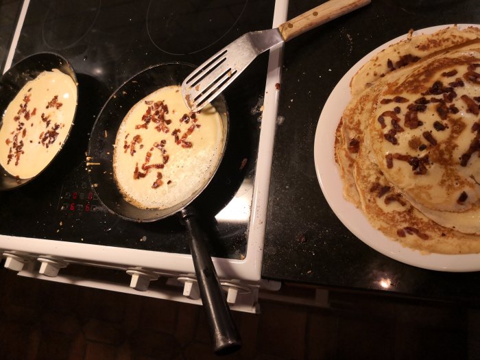 Pannkakor med inbakat fläsk steks på spis och en tallrik med färdiga pannkakor.